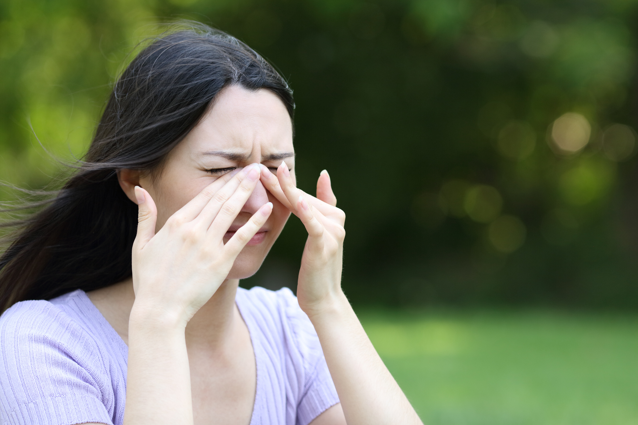 Woman scratching itchy eyes in a park.
