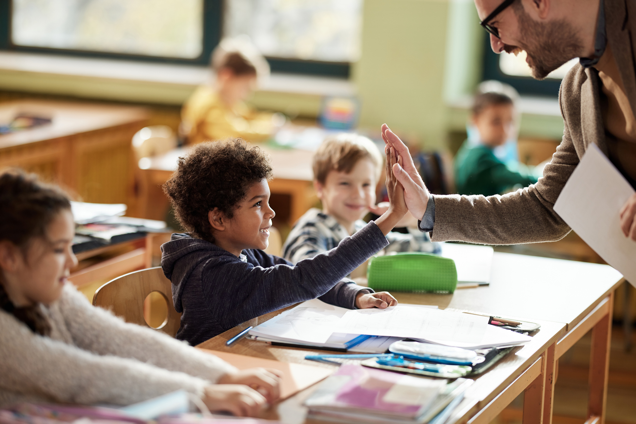 Happy male teacher giving high-five to his elementary student on a class in the classroom.