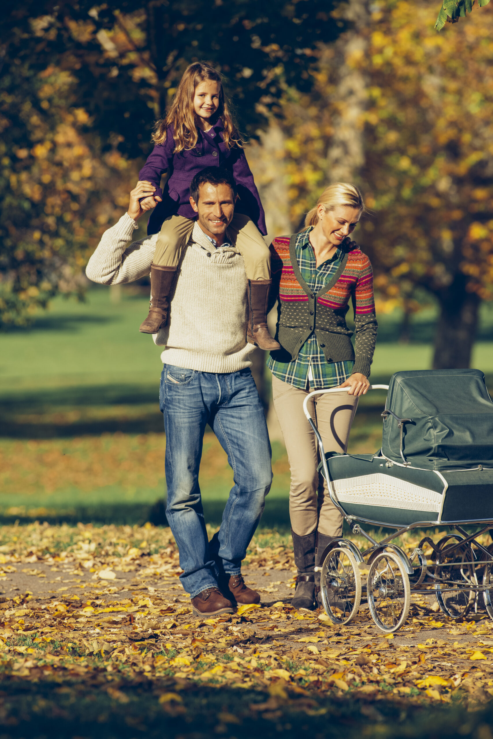 Family with baby carriage enjoying walk at the autumnal park